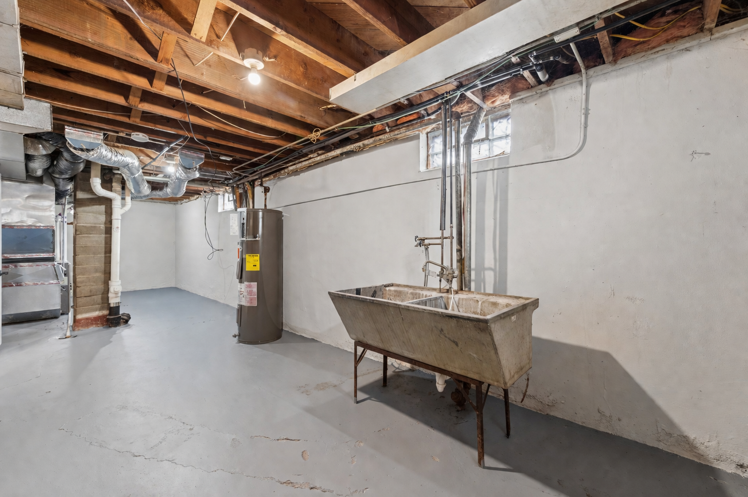 Unfinished lower level offers great utility space with painted floors, exposed mechanicals, and a large utility sink—perfect for laundry, storage, or workshop use.