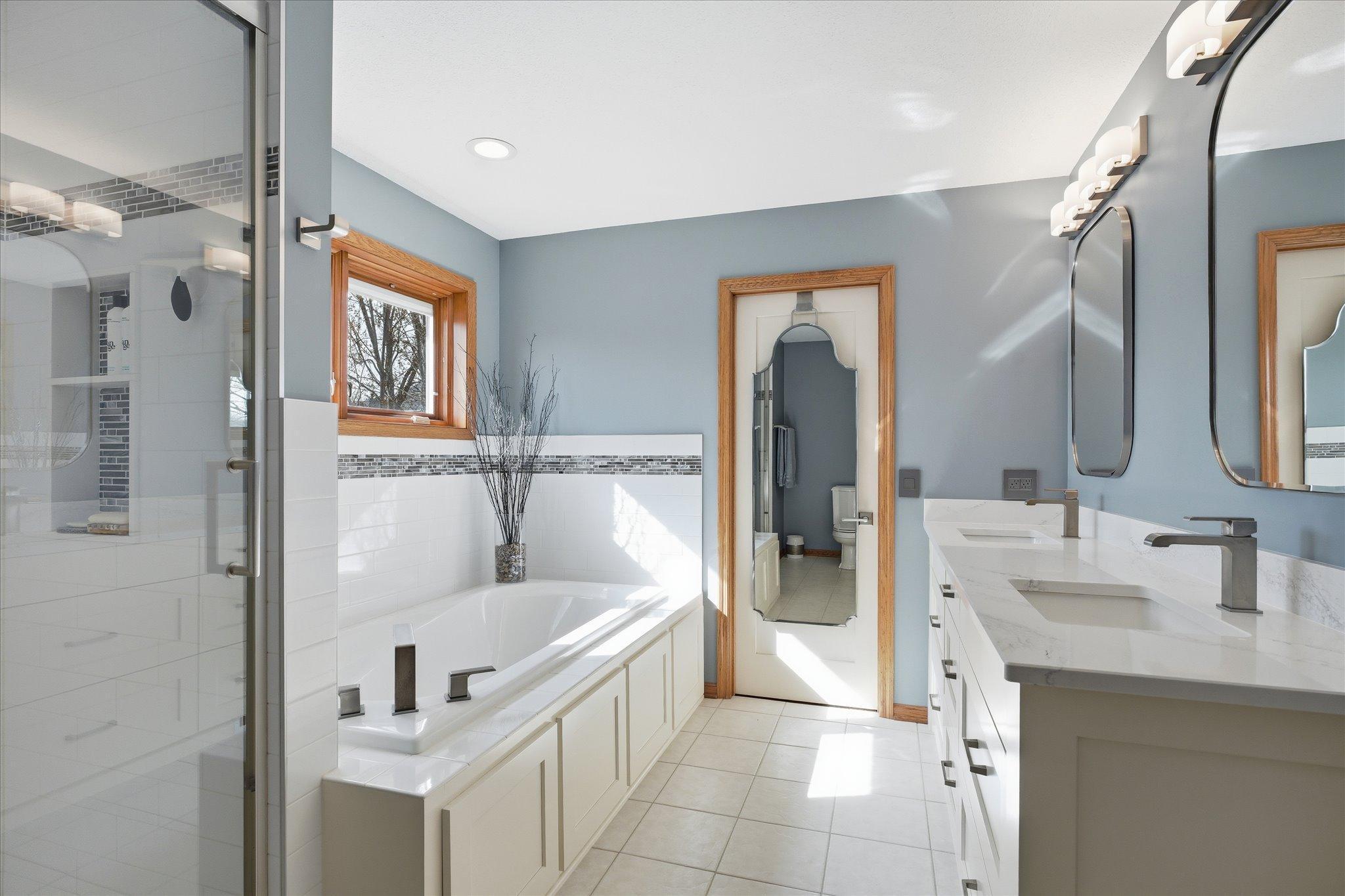 Remodeled primary bath featuring a dual vanity with Cambria countertops, ceramic tile shower and flooring.