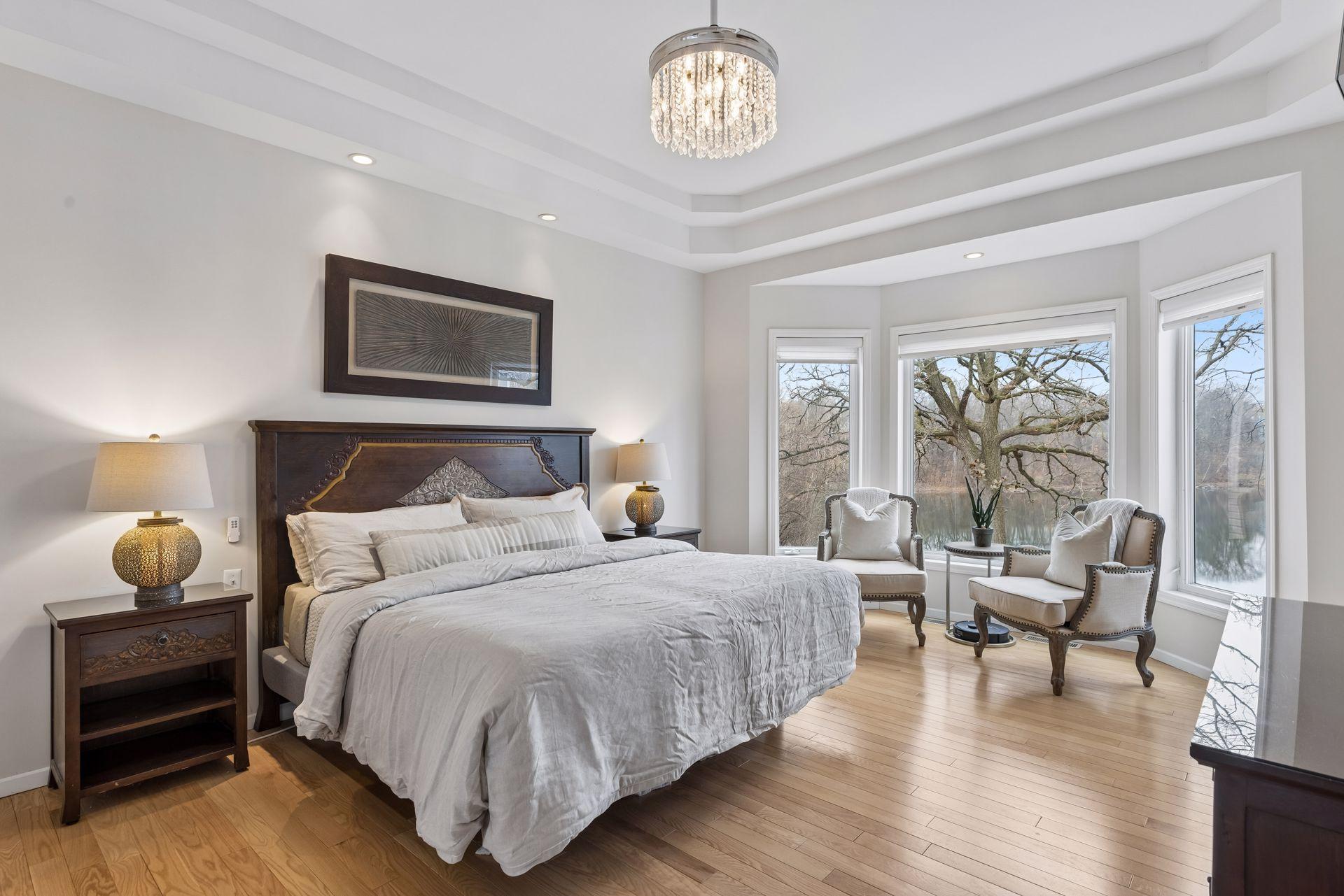 This serene retreat features a tray ceiling, warm hardwood floors, and an elegant chandelier that adds a touch of sophistication. A wall of oversized windows frames a peaceful, tree-lined lake view.