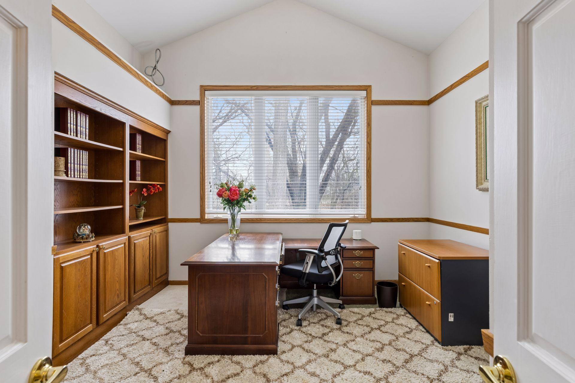 Bright and inviting main-floor office featuring a vaulted ceiling, oversized window, and custom built-in cabinetry. New carpet will be installed in the office Friday, 4/17.