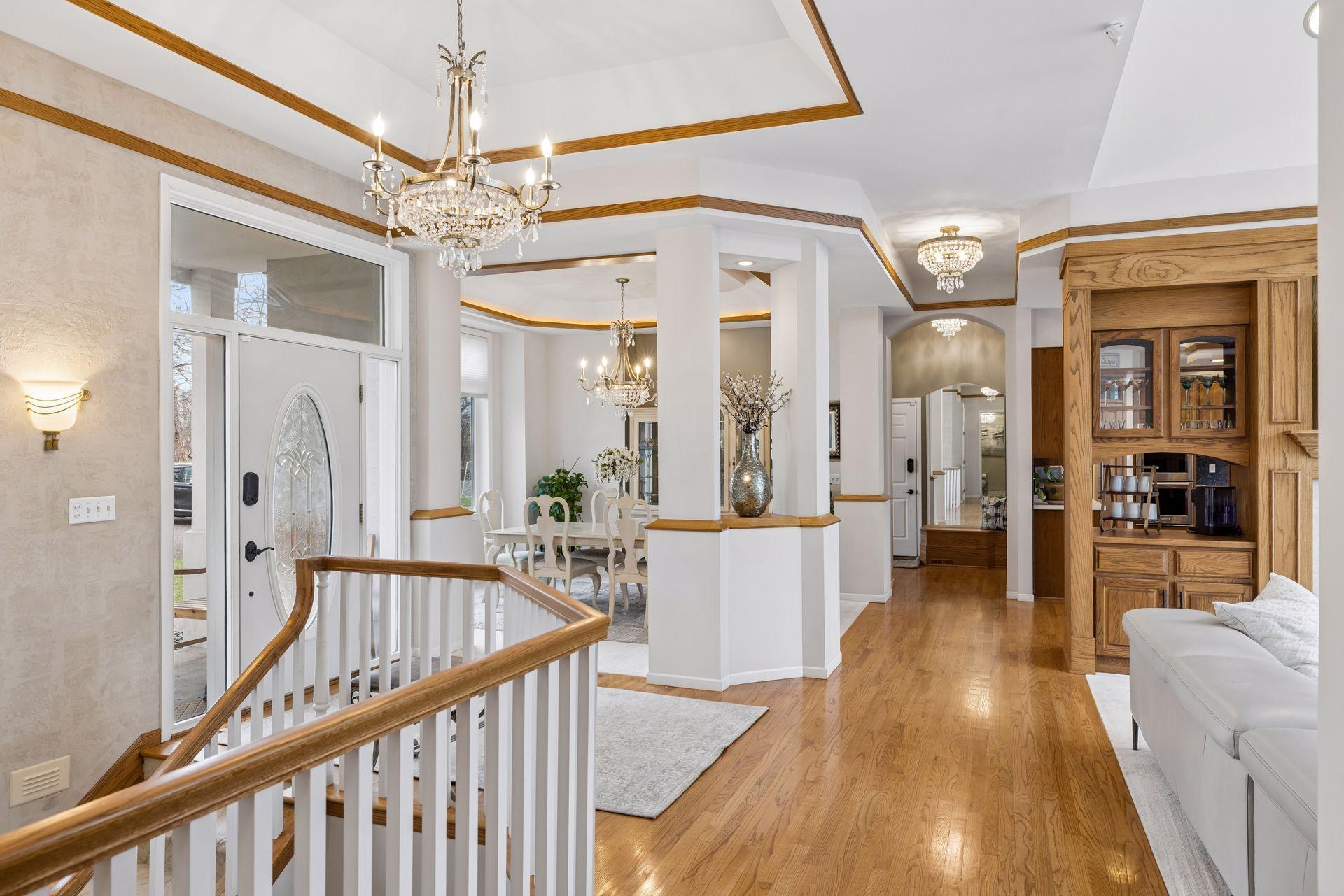 The open-concept layout is enhanced by decorative columns, tray ceilings with crown accents, and stunning chandelier lighting that adds warmth and sophistication.