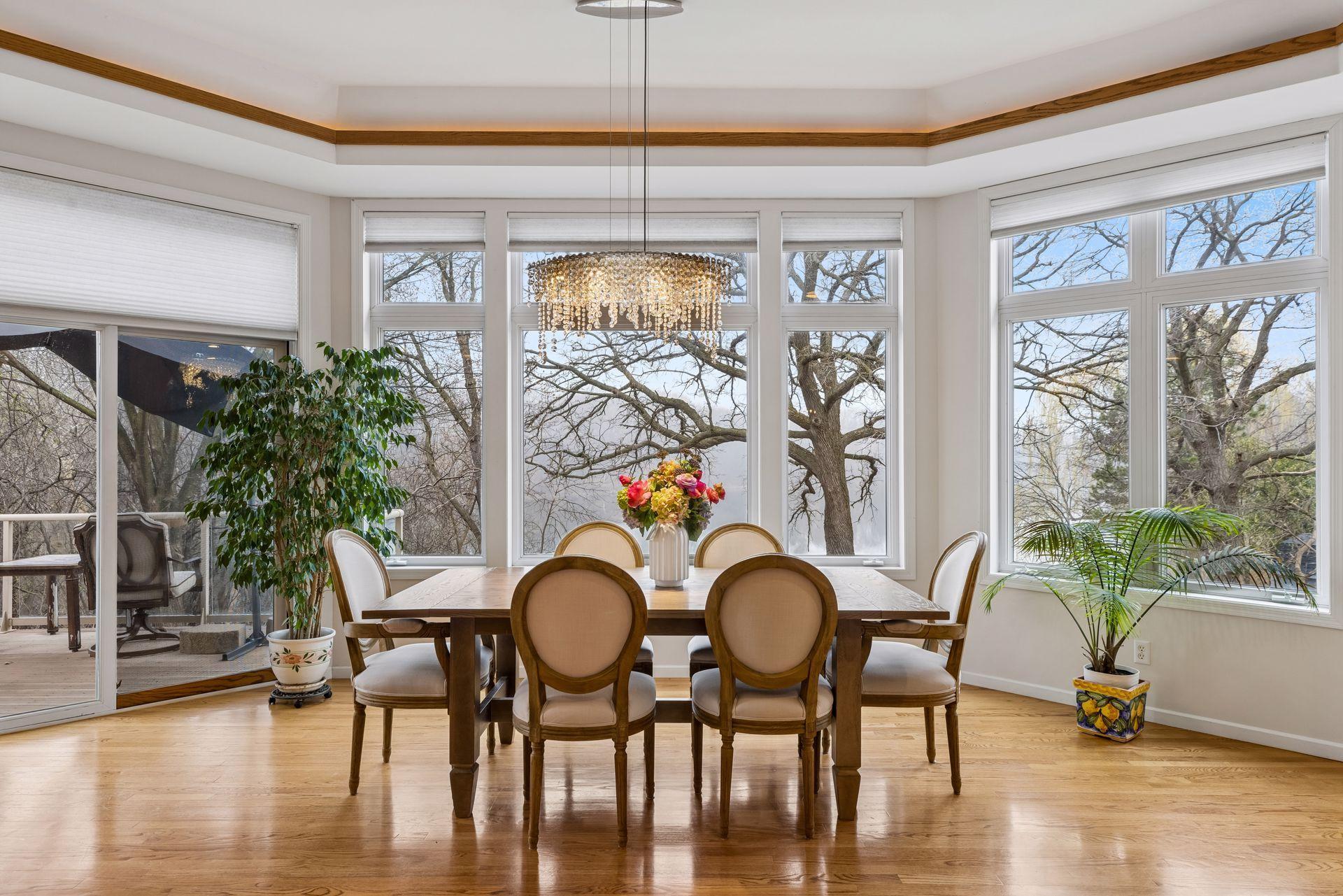 The adjoining dining area is surrounded by expansive windows that fill the room with natural light and showcase peaceful, tree-lined views with glimpses of the water beyond.