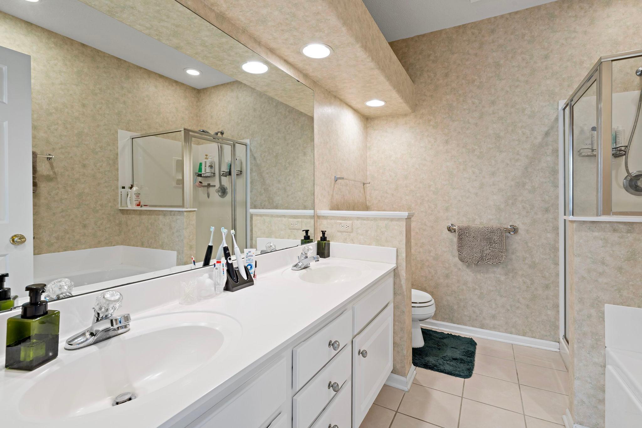 The owner’s bathroom features dual sinks and a spacious walk-in shower with a separate jetted tub for added luxury.