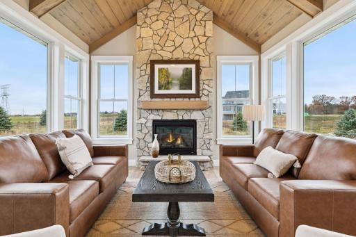 Stone fireplace anchors sunroom with rustic charm, vaulted wood ceiling, and abundant natural light.