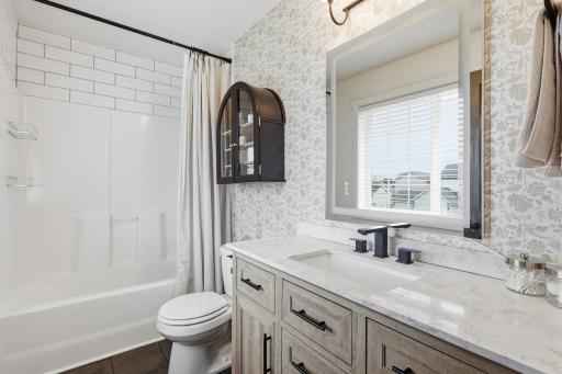 Updated primary bathroom with tile floors, long vanity with space to get ready, updated mirror and light fixtures. Tile accents above shower.