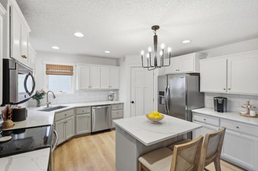 Updated kitchen with quartz countertops, tile backsplash, enameled cabinetry, center island with seating, stainless steel appliances, and walk-in pantry, and tons of counterspace.