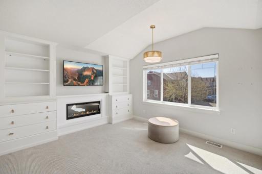 Vaulted ceilings and large windows create an airy, light-filled atmosphere, while a cozy gas fireplace and custom built-ins add warmth and character.