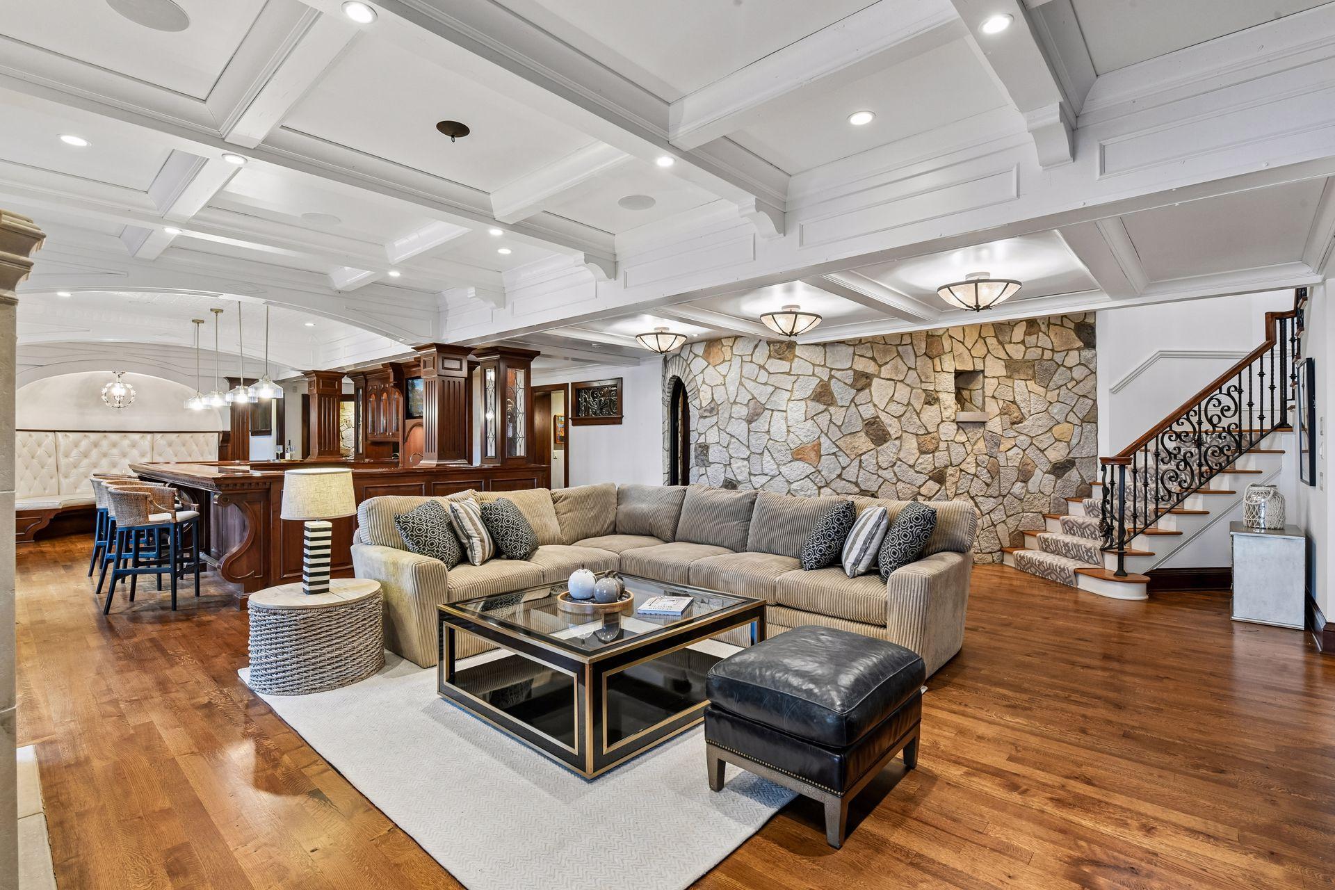 Lower level family room is located at the base of the steps, large stone wall, wood floors and bright white stylized paneled ceilings blend many materials that come together beautifully