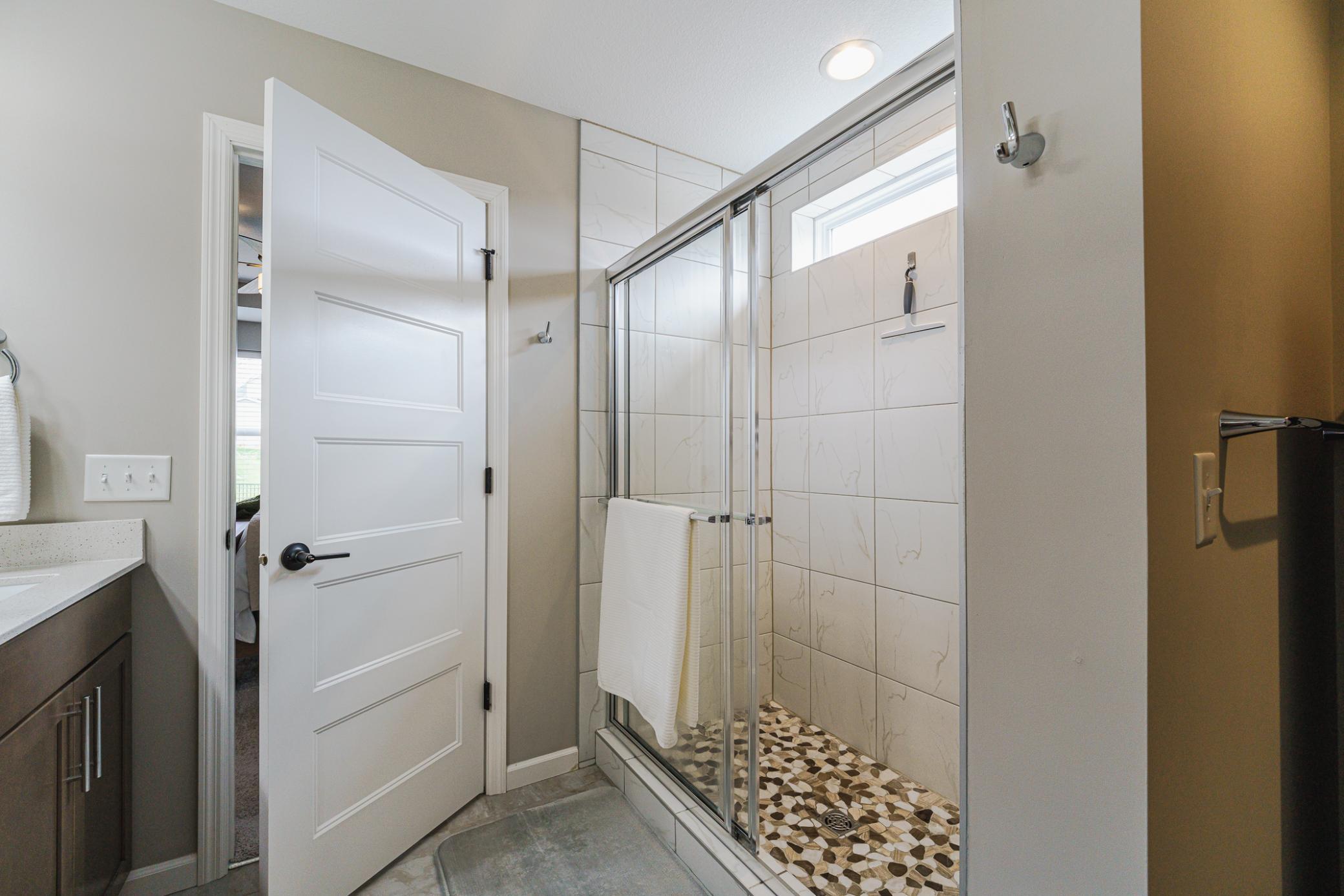 The bathroom showcases a tile shower with “pebble-style” flooring and a bright transom.