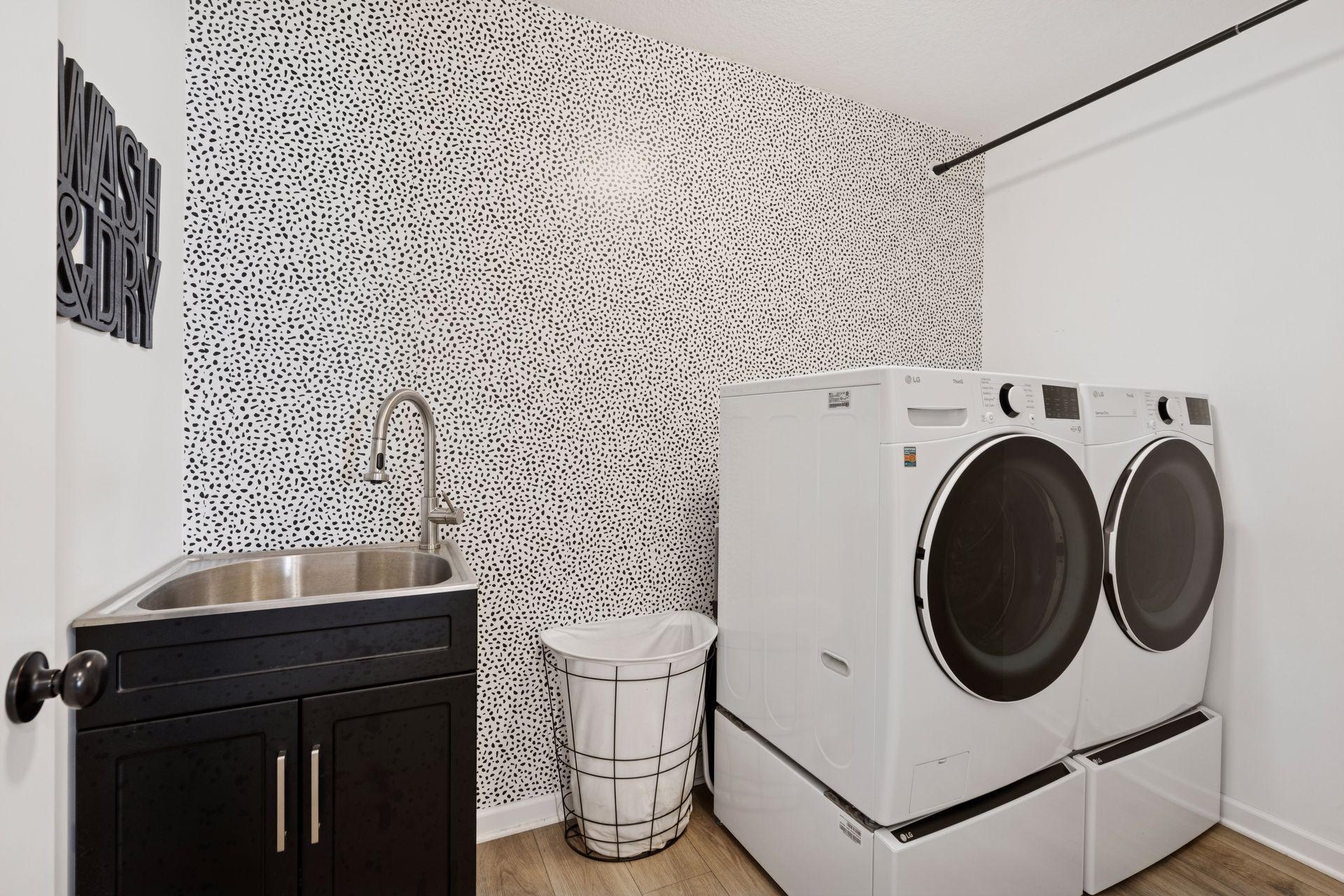 Recently finished laundry room with accent wallpaper, new slop sink, and hanging for clothes.