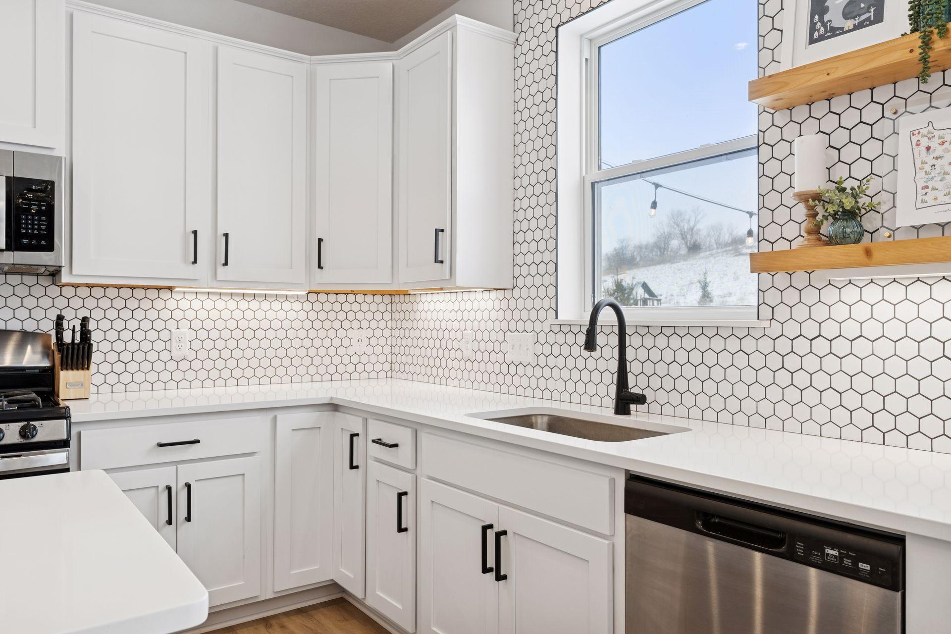 Hardwired under cabinet lighting, recently finished tile backsplash, large under mount kitchen sink, and floating shelving next to window.