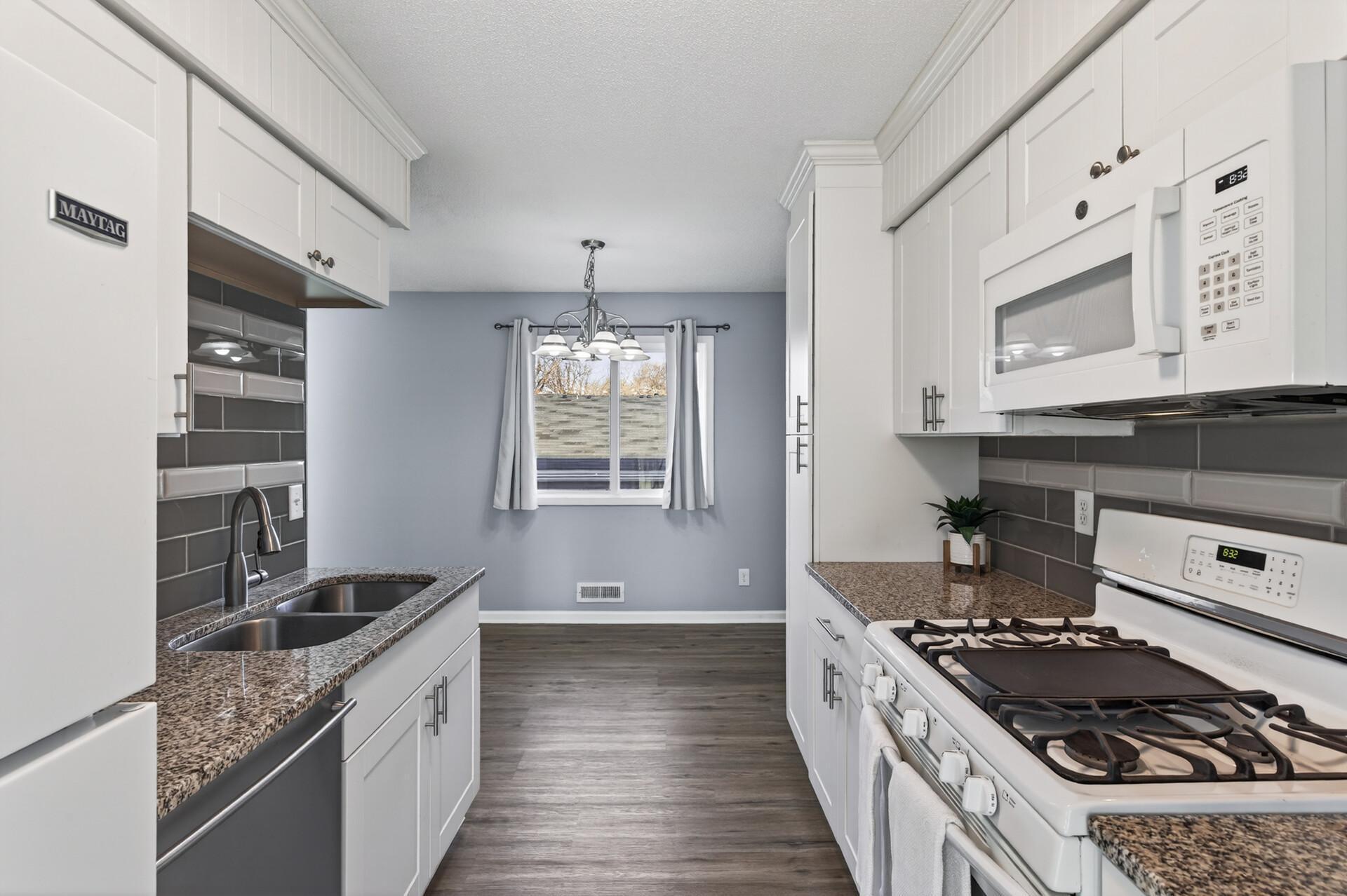Alternate view of the remodeled kitchen showcasing abundant cabinet storage, gas range, built-in microwave, and seamless flow into the dining area.