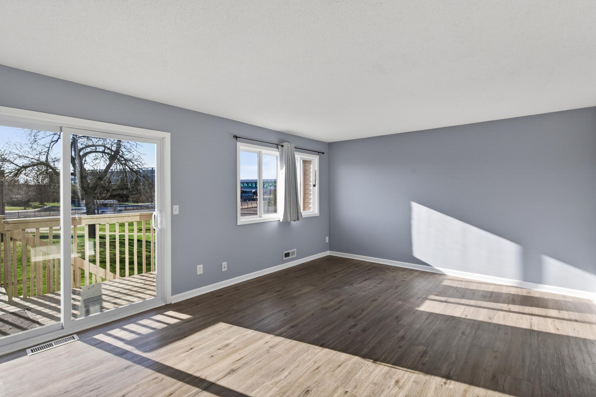 Sun-filled upper-level living room with updated flooring, neutral paint, large windows, and sliding glass door leading to the private deck.