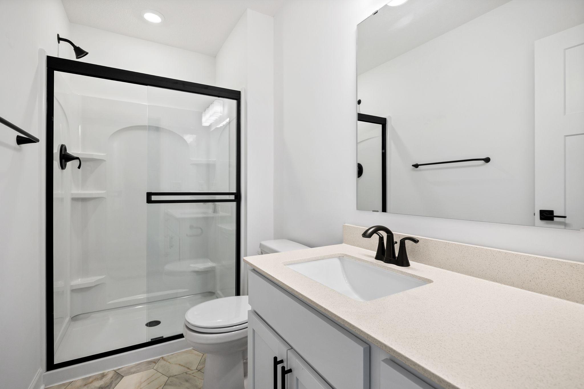 (Photo of a similar home, actual finishes may vary) This bathroom is discreetly located down a hallway off the foyer, offering access to a single vanity and glass-enclosed shower.