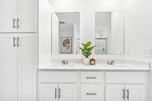 (Photo of model home, features will vary) Featuring a glass-enclosed shower with built-in shelving and glass mirrors set atop dual quartz sinks and vanity-cabinetry, the en-suite bathroom helps streamline morning routines