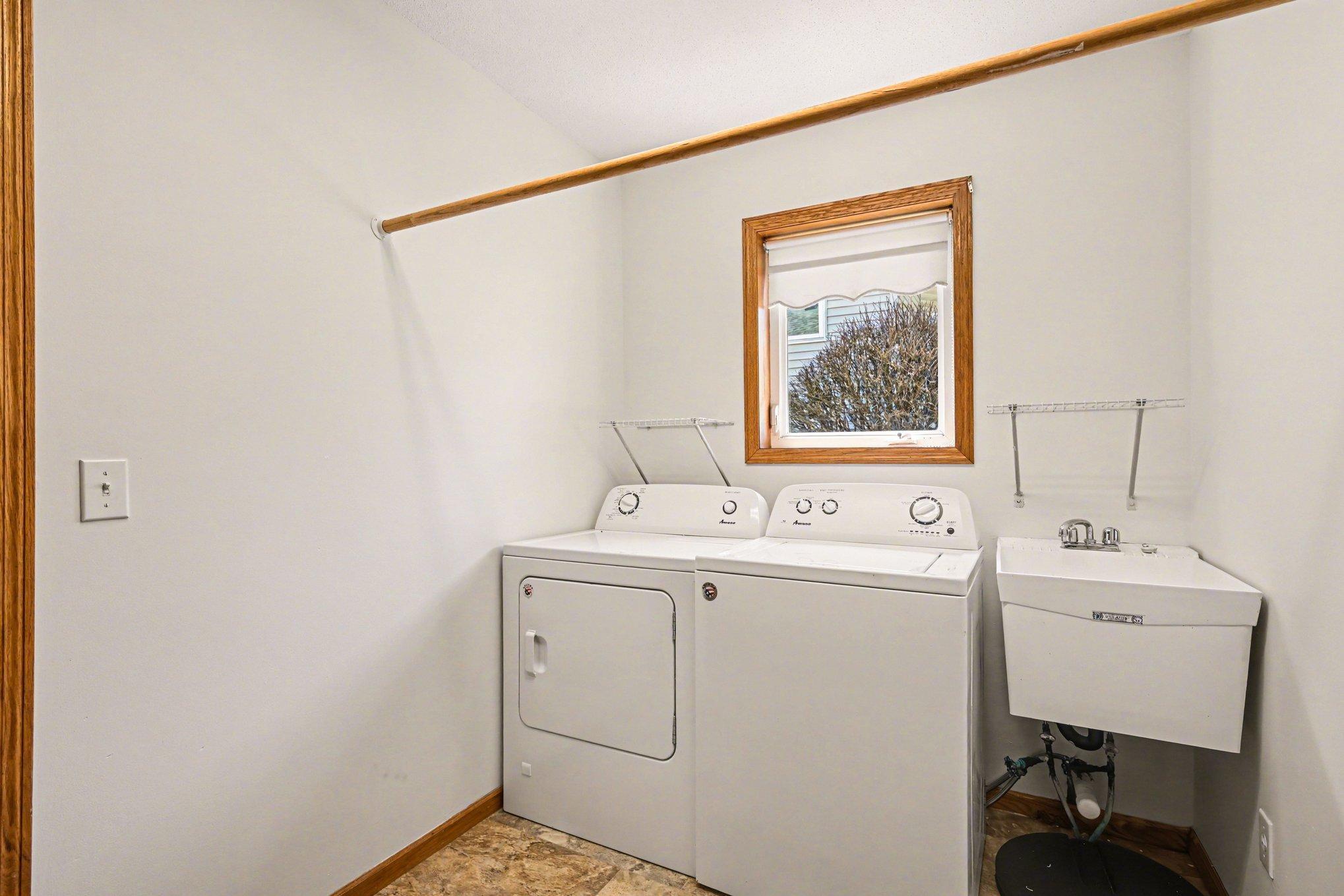 This laundry/mudroom features a washer, dryer, utility sink, and hanging rod. Located between the garage and kitchen, the efficient layout and extra coat closet make unloading groceries a breeze. Functional one-level living at its best!