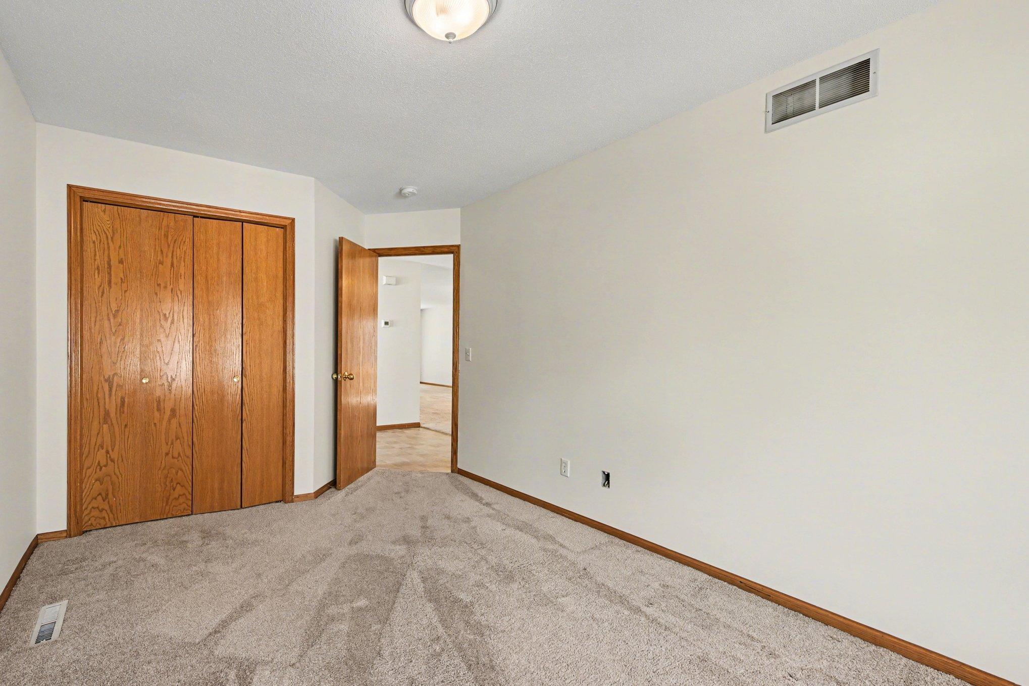 This view highlights the second bedroom's large closet and easy access to the home's entryway. Freshly painted and filled with natural light, this versatile room is perfectly positioned for use as a guest suite or a quiet home office.