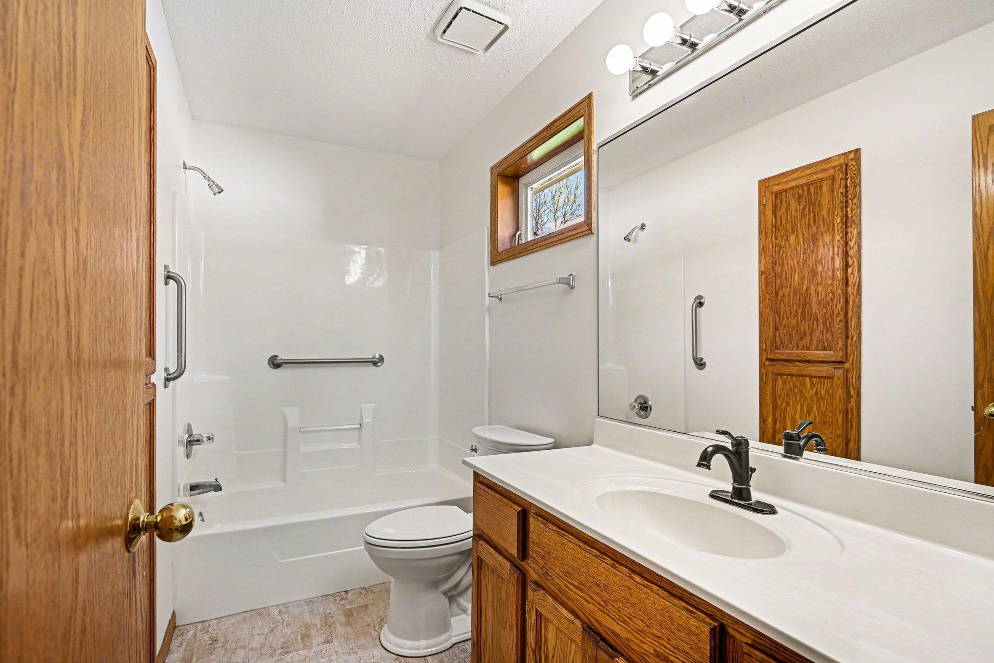 The private primary bath features a large vanity, transom window, and tub with grab bars. With a two-level linen closet for easy organization, this space perfectly combines style and function. Clean, bright, and ready for your morning routine!