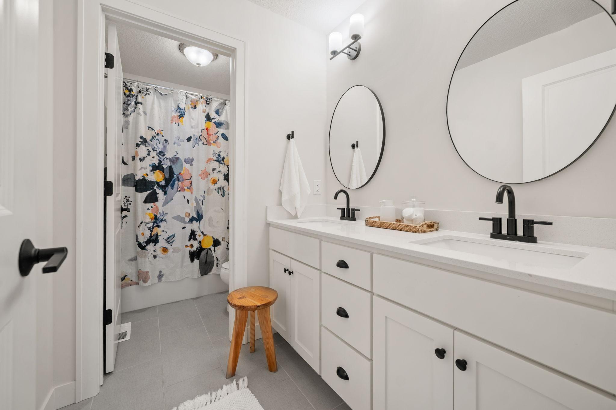 Full Bathroom on the Upper Level features enameled vanity cabinet with quartz countertop & dual sinks, modern tile flooring + separate room for tub and commode