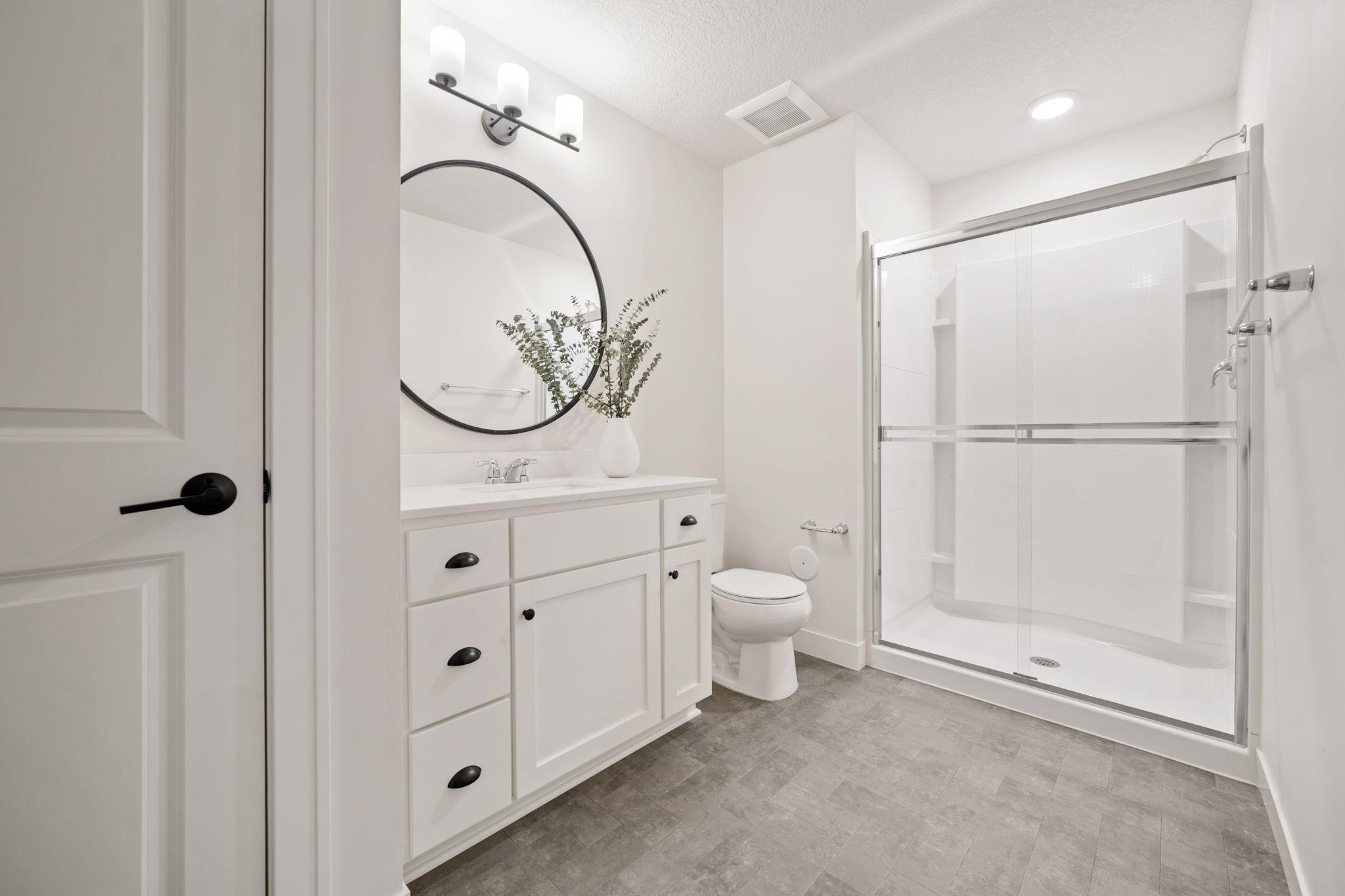 3/4 bathroom in the Lower Level features enameled vanity cabinet with quartz countertop, glass shower doors and linen closet