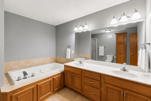 Relax and unwind in the spacious primary bath featuring a jetted soaking tub, dual-sink vanity, and ample cabinet storage.