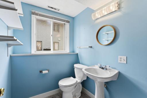 Soft blue walls and a pedestal sink keep this lower-level bath light and easy, with a round mirror and easy-care plank flooring for low-maintenance everyday use.