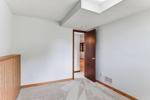 This room opens into the lower-level hall, with carpet, wood trim, and daylight pulling through from the adjacent rooms.