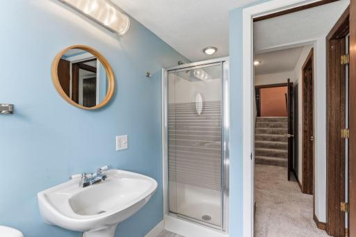 A glass-door shower turns the lower-level bath into a true three-quarter bath, paired with a pedestal sink and quick access to the carpeted hall just outside.
