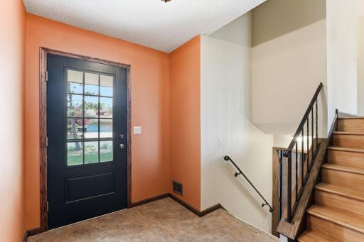 A glass-paneled entry door pours morning light into the tile foyer, with the stairs lifting just beyond to the main level.