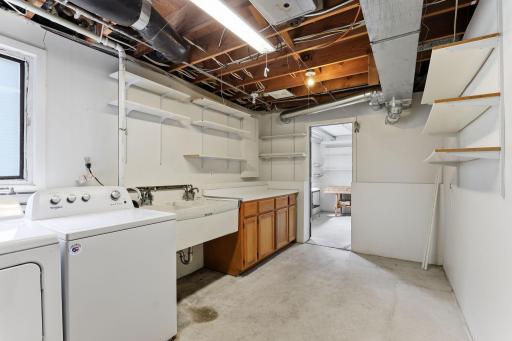 Laundry, a deep utility sink, and generous shelving fill the lower-level utility room, with pass-through access to the workshop next door.