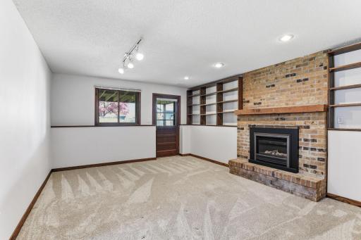 Brick climbs floor to ceiling around the gas fireplace in the lower-level living room, flanked by built-in shelves and lit by overhead track lighting.