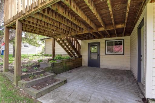 Below the deck, a covered concrete patio offers shade, easy outdoor seating, and direct walkout access to the lower-level entry.