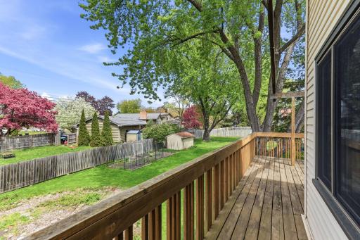 Looking out from the deck rail, the fenced backyard, garden plot, tidy shed, and mature trees fill the view.