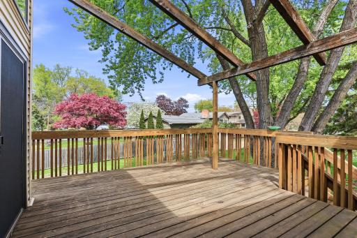 From the deck, mature trees, spring blooms, and the fenced yard fall into easy view through an overhead pergola-style canopy.