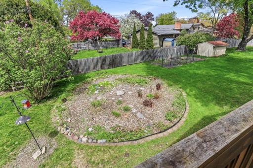 From above, the backyard reveals a circular planted bed, a vegetable garden, mature trees in bloom, and clear sight lines across the fenced yard.