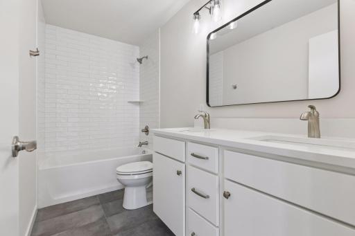 Upper-level 2nd bathroom with double vanity, quartz countertops, and soft-close cabinetry. Tiled shower/tub combo offers both style and everyday functionality.