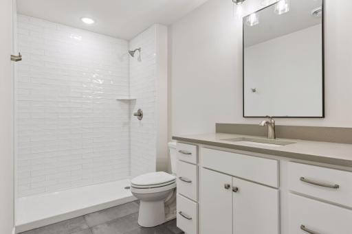 Lower-level 3/4 bathroom featuring tile flooring, tiled shower walls, and soft-close cabinetry. Clean, modern finishes with a functional layout - ideal for everyday use and guest convenience.