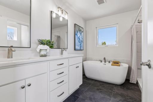 Full primary bathroom featuring a modern soaking tub, separate shower, and tiled flooring. Double vanity with quartz countertops and soft-close cabinetry offers both style and functionality in a well-designed space.