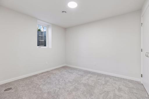 Private fifth bedroom on the lower level with egress window, soft carpeting, and closet - ideal for guests, in-laws, or home office.