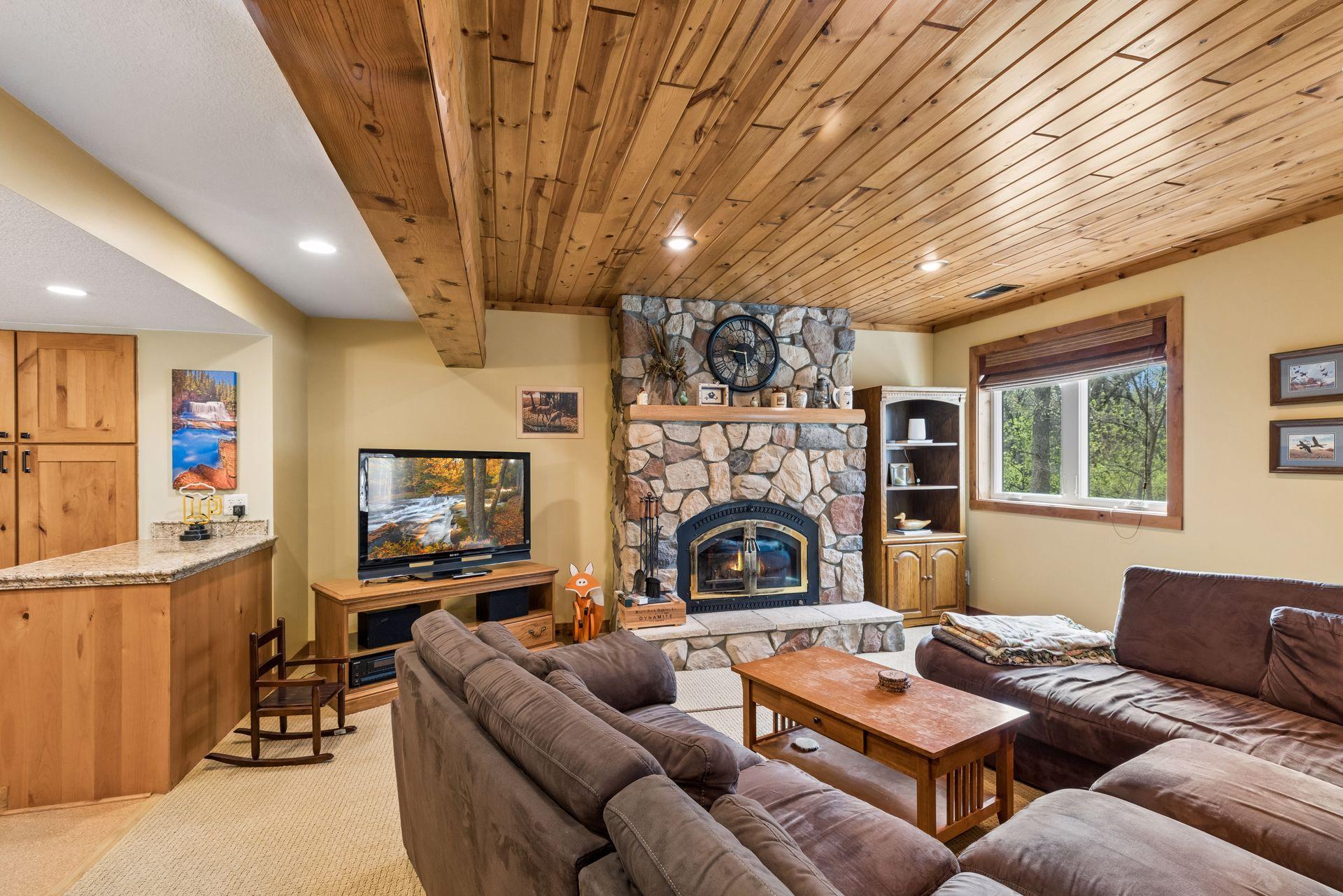 Warm, rustic lower level with wood ceilings and a stone-surround wood-burning fireplace.