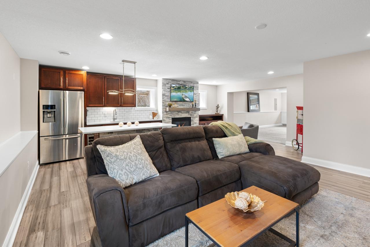 Fantastic 23x24 lower-level recreation room featuring a bar area with full-size refrigerator, wine cooler, custom cabinetry, and large island with quartz countertops, plus a separate seating area with a gas fireplace.