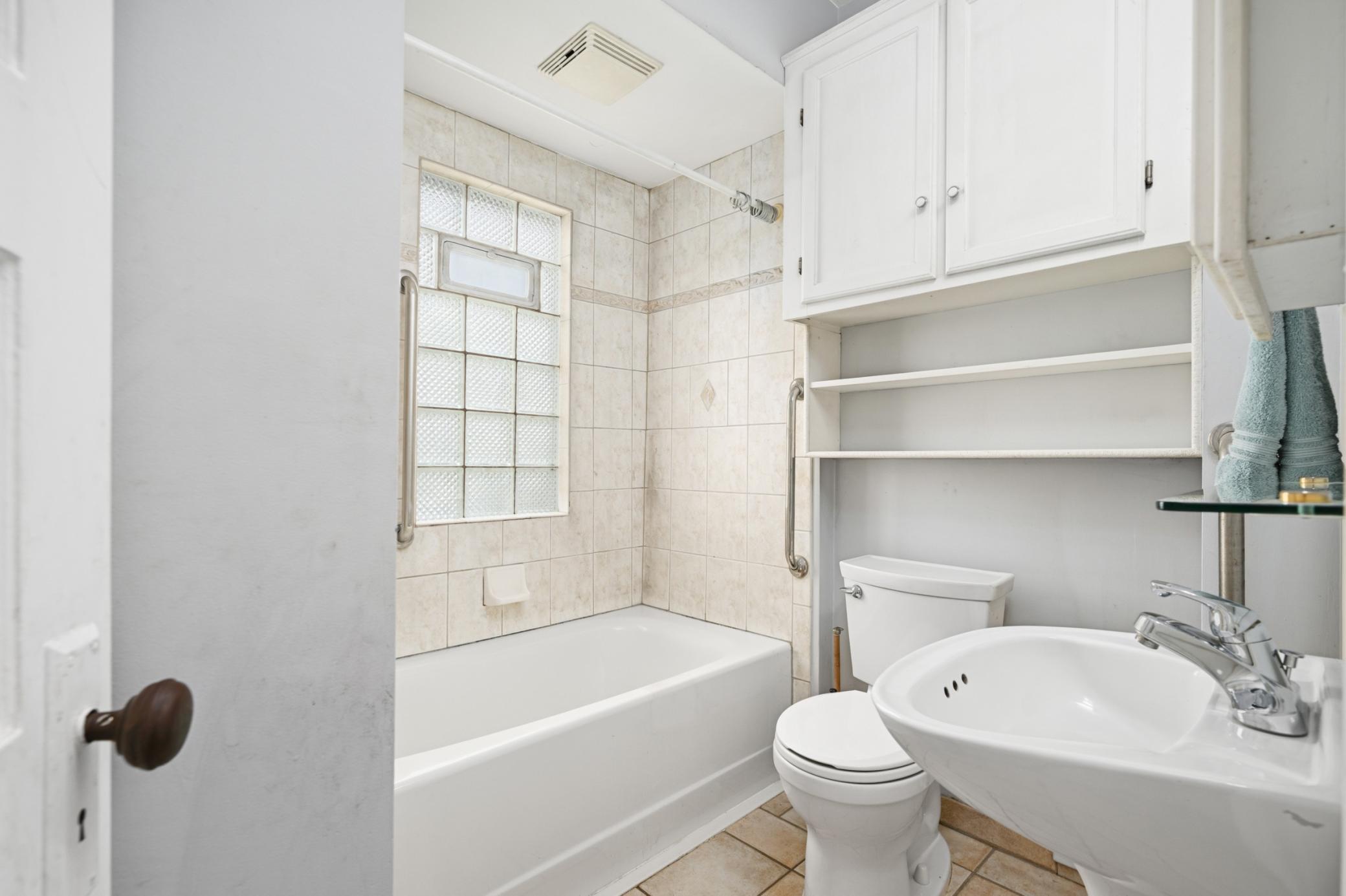 Main floor full bathroom with glass block window and ceramic tile.