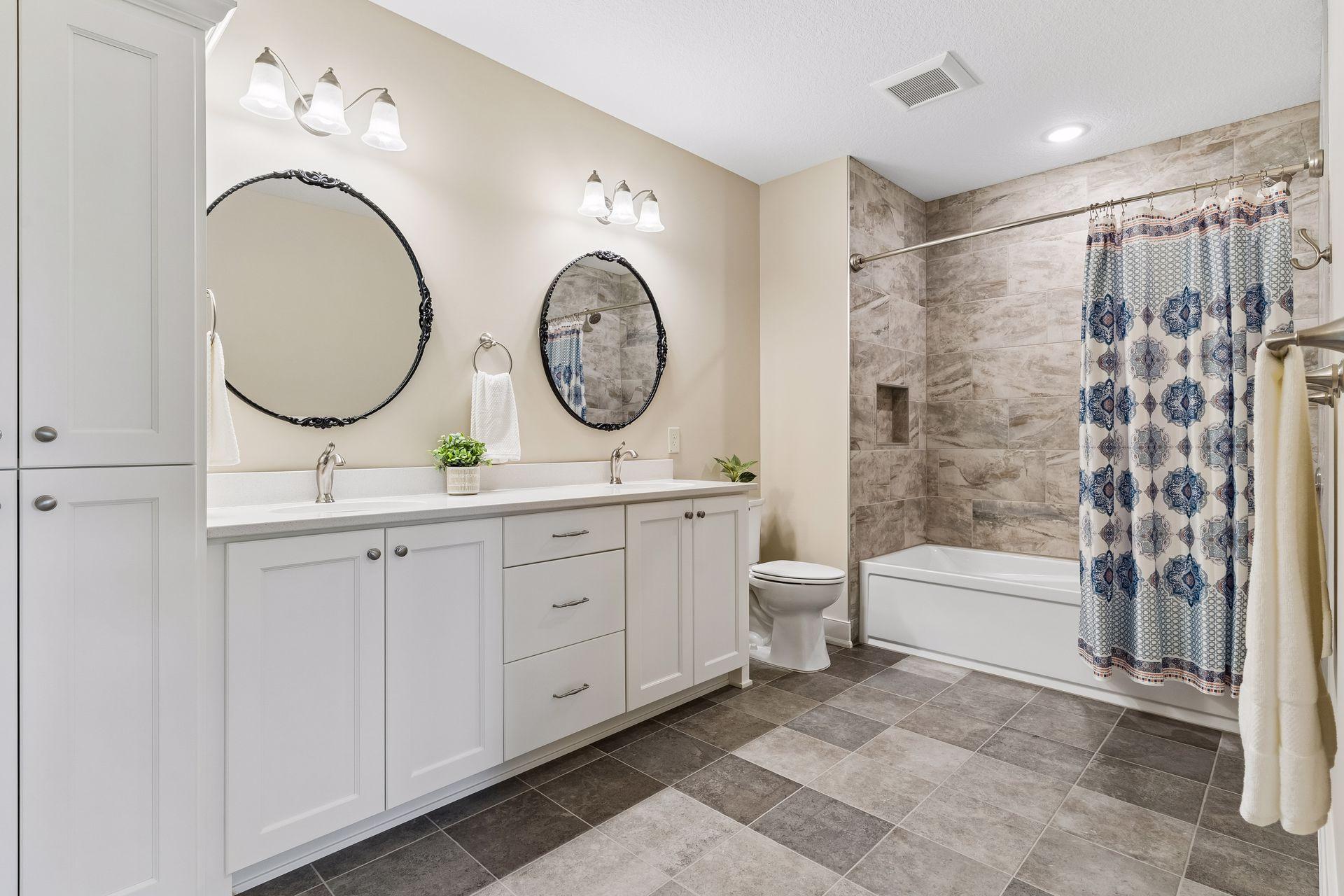 The lower-level full bath features a double vanity, tiled tub/shower surround, and convenient placement near the bedrooms, theater, and recreation spaces.