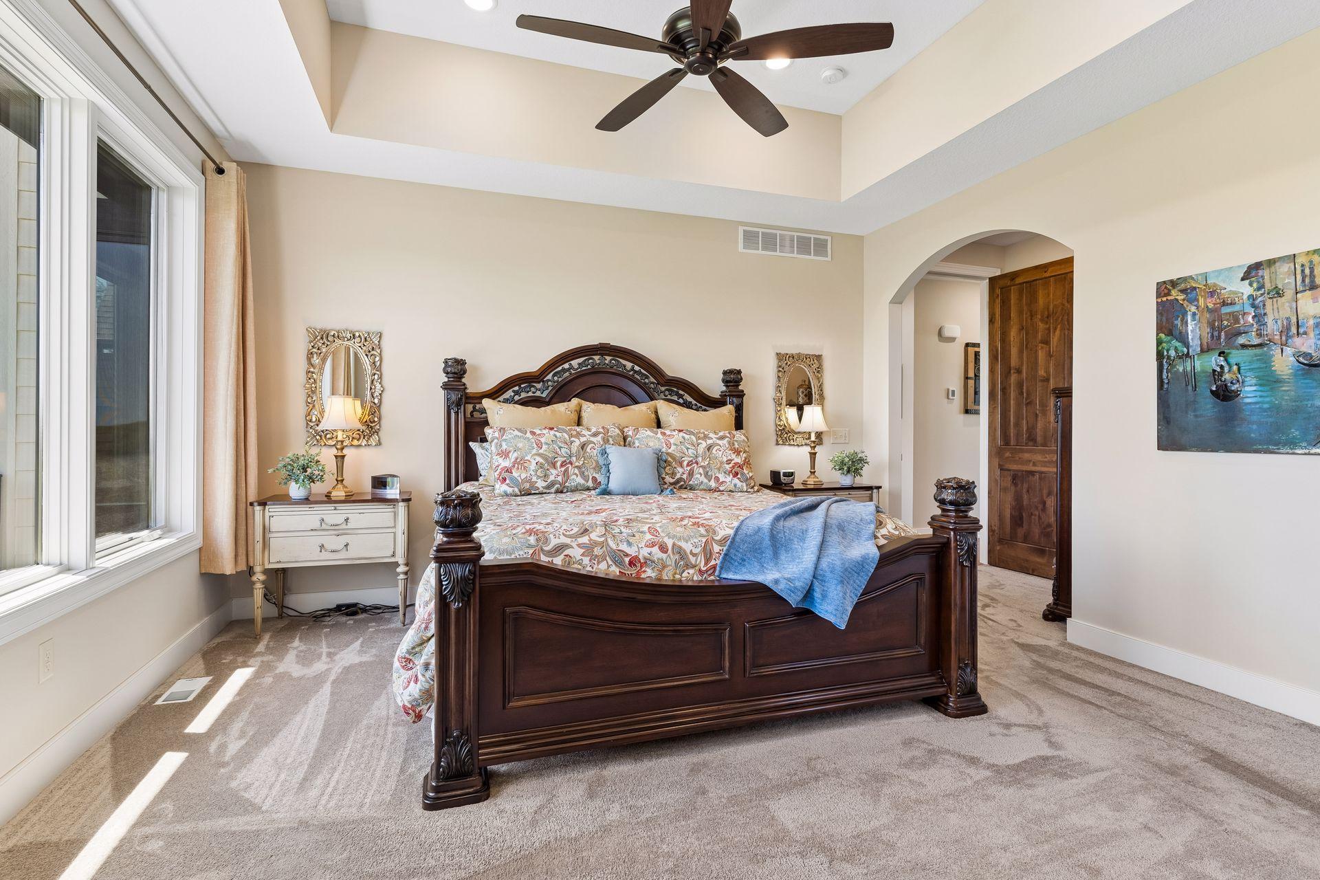 The south-facing primary suite is filled with natural light and features large windows, a vaulted tray ceiling, ceiling fan, heated floors, and a spacious layout designed for comfort and privacy.