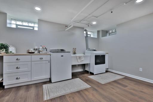 Bright, finished lower level featuring a spacious laundry suite. Boasts custom white cabinetry, ample counter space, and durable wood-look flooring. A clean, organized area with plenty of storage.