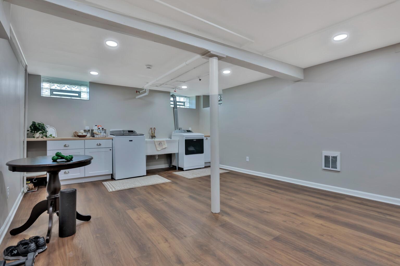Bright, finished lower level featuring a spacious laundry suite. Boasts custom white cabinetry, ample counter space, and durable wood-look flooring. A clean, organized area with plenty of storage.