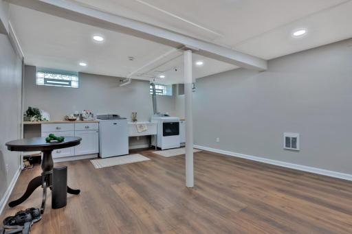 Bright, finished lower level featuring a spacious laundry suite. Boasts custom white cabinetry, ample counter space, and durable wood-look flooring. A clean, organized area with plenty of storage.