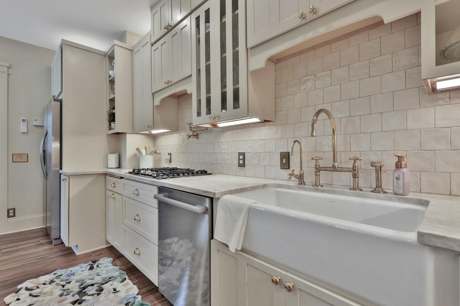Stunning kitchen boasting leathered natural stone, professional enameled cabinets, & brass hardware. Includes a farmhouse sink, bar prep area with chiller, & tile backsplash over heated wood-look ceramic floors.