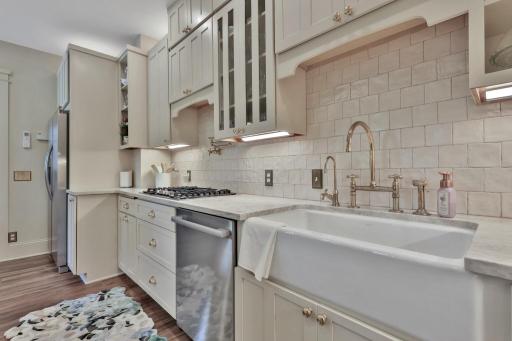 Stunning kitchen boasting leathered natural stone, professional enameled cabinets, & brass hardware. Includes a farmhouse sink, bar prep area with chiller, & tile backsplash over heated wood-look ceramic floors.