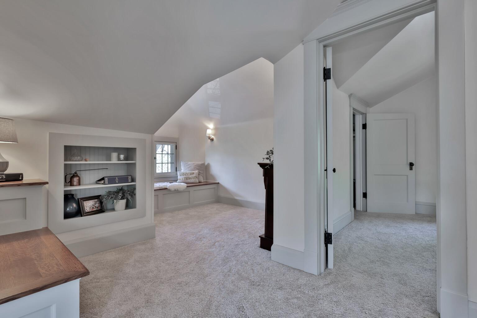 Discover your new favorite retreat! This cozy reading area features custom built-in shelving and a sun-drenched window seat, all tucked under charming sloped ceilings for a true sanctuary feel.